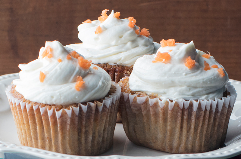 three carrot cake cupcakes on a white serving dish