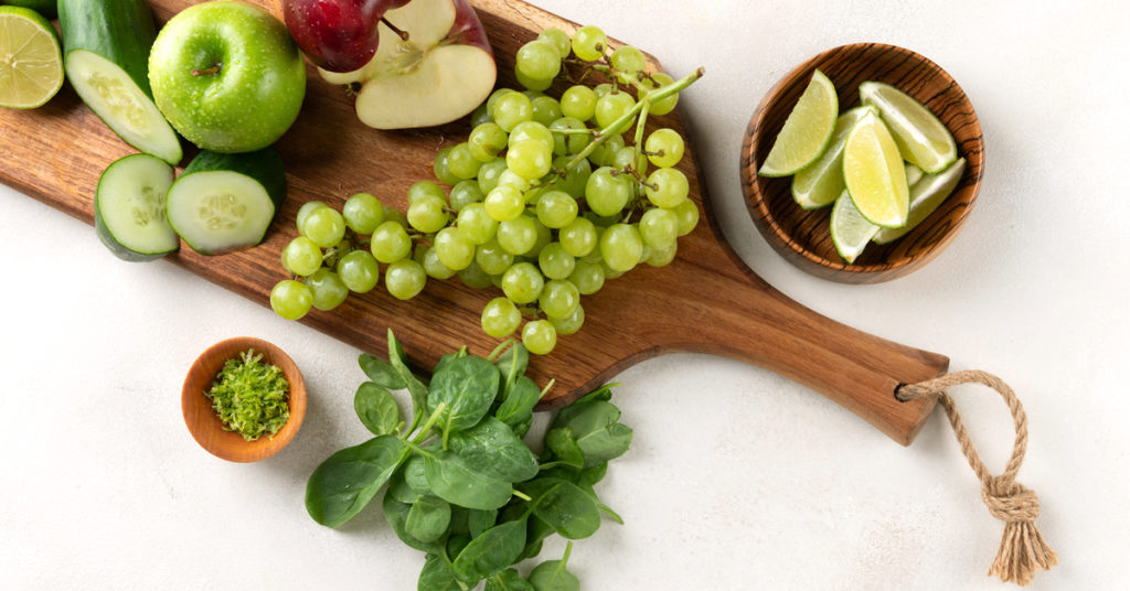 Ingredients apple, grapes, spinach and lime on a wooden cutting board