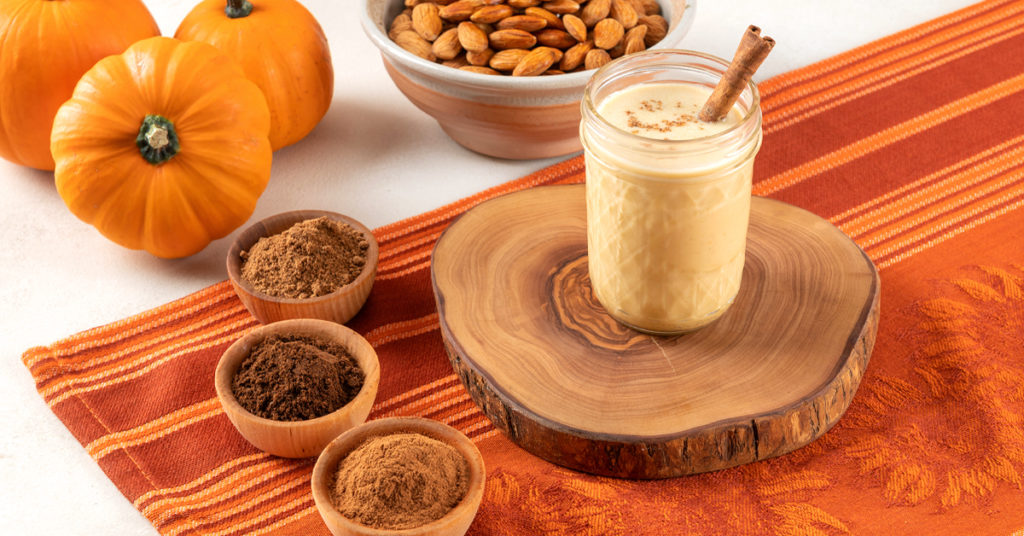 one glass of homemade pumpkin pie milk on a wooden slab surrounded by ingredients
