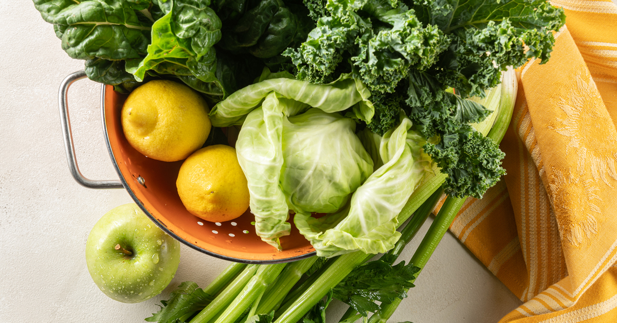 ingredients to make green cabbage juice, lemon, apple, celery, kale in a colander
