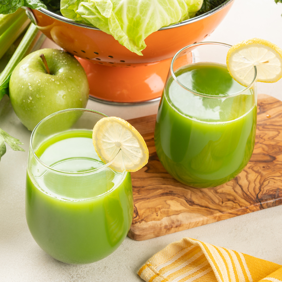 two glasses of green juice with ingredients, cabbage, apple, celery, lemon