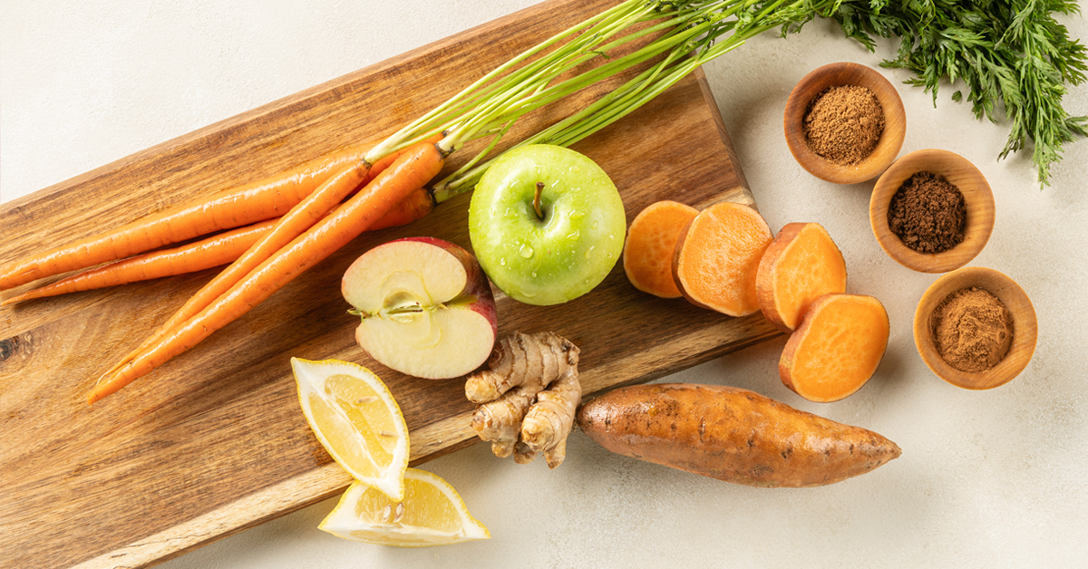 Ingredients for making sweet potato juice, apple, carrot, ginger, lemon, clove cinnamon and nutmeg on a wooden cutting board