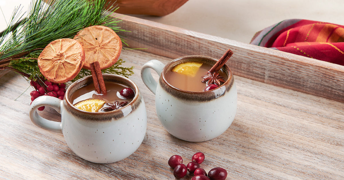 two mugs of warm apple cider on a wooden serving tray
