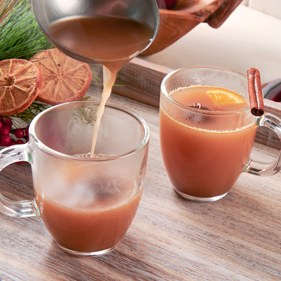 pouring hot apple cider into glass mugs for serving