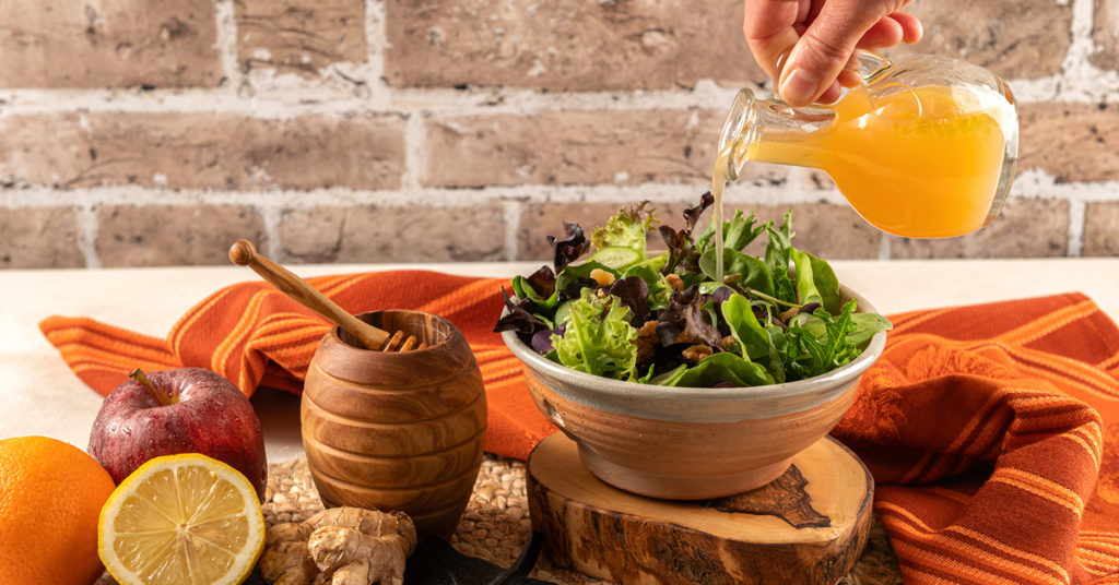 pouring fall dressing on a salad on a wooden serving platter