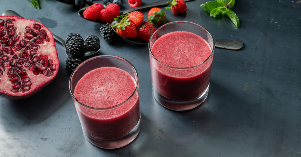 two glasses of berry juice on a slate background