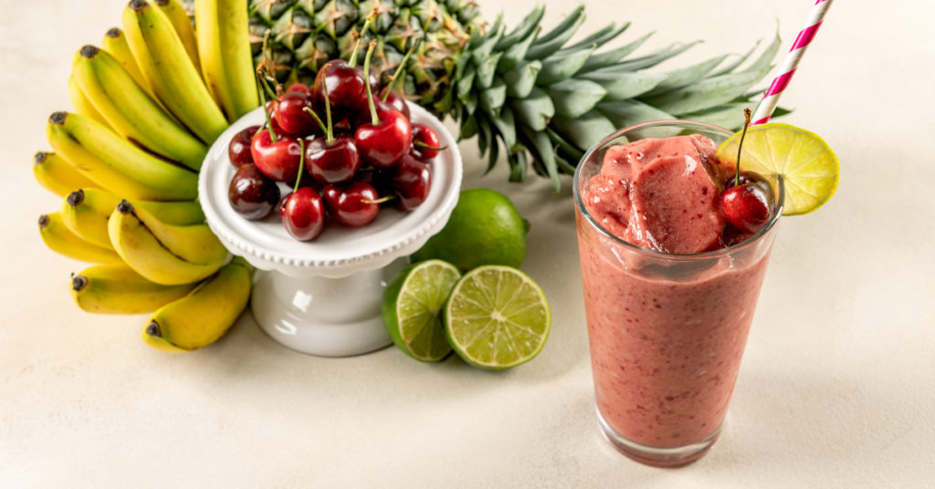 tropical guava smoothie on a table surrounded by ingredients, cherry, lime, banana, pineapple and lime