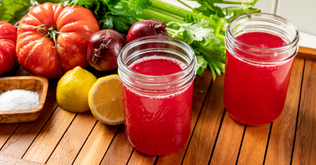 two jars of tomato juice with ingredients to make the recipe on a wooden tray