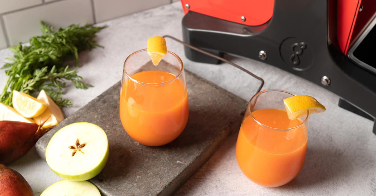 jugo de abc de zanahoria y remolacha de manzana junto a un exprimidor en una mesa