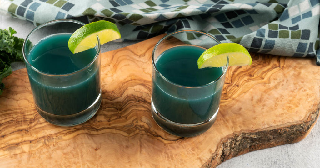 two glasses of kale juice on a wooden cutting board