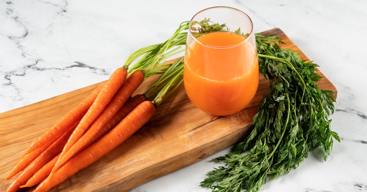 a glass of carrot juice and carrots on a cutting board